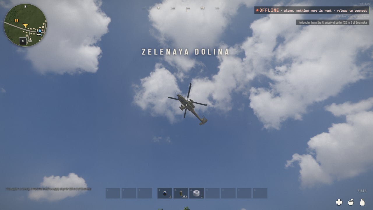 Looking straight up at an Apache gunship hovering against blue sky and white clouds, its rotor blades spread