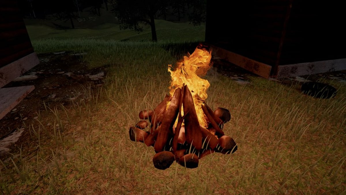 A campfire at night beside a log cabin: a pile of logs glowing where they burn, tall yellow flames over them, and the grass round it lit orange