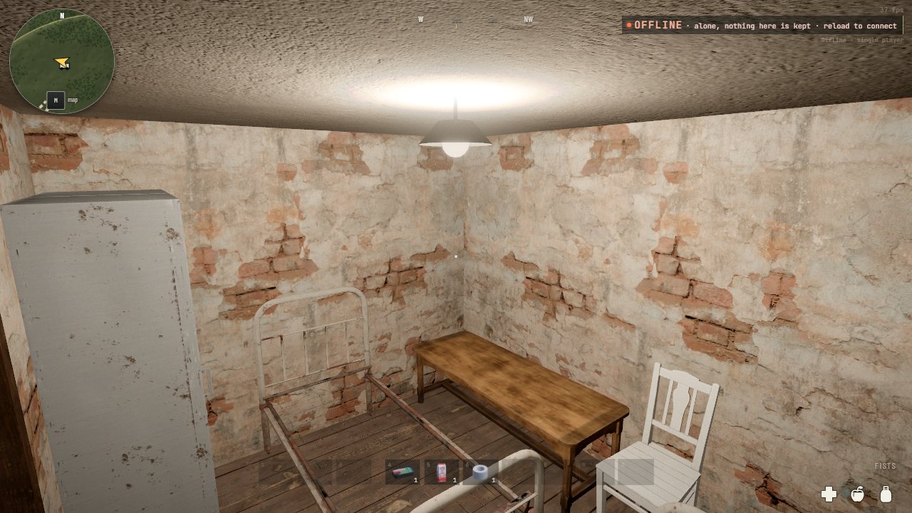 A plastered room with a bed frame, a table, a chair and a steel locker under a hanging bulb