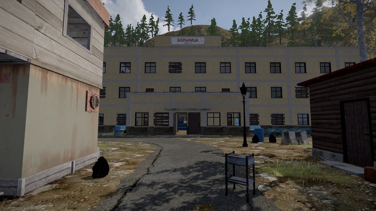 Seen from the street between two houses: a long hospital of three floors in pale yellow plaster with white bands, a block built out before its doors, a sign over the roof reading Bolnitsa, Hospital, a lamp post and a concrete barrier on the drive