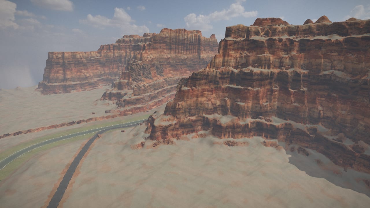 The canyon country from 80 m up: red cliffs in layered beds, rock fallen at their feet, the road below