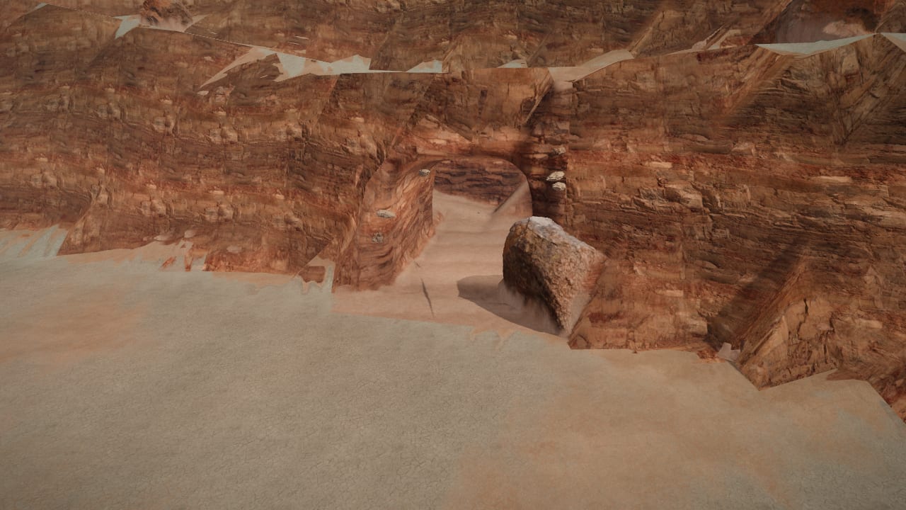 A cave mouth in the pass's red wall, recessed into the rock, a fallen block beside it and the way in clear
