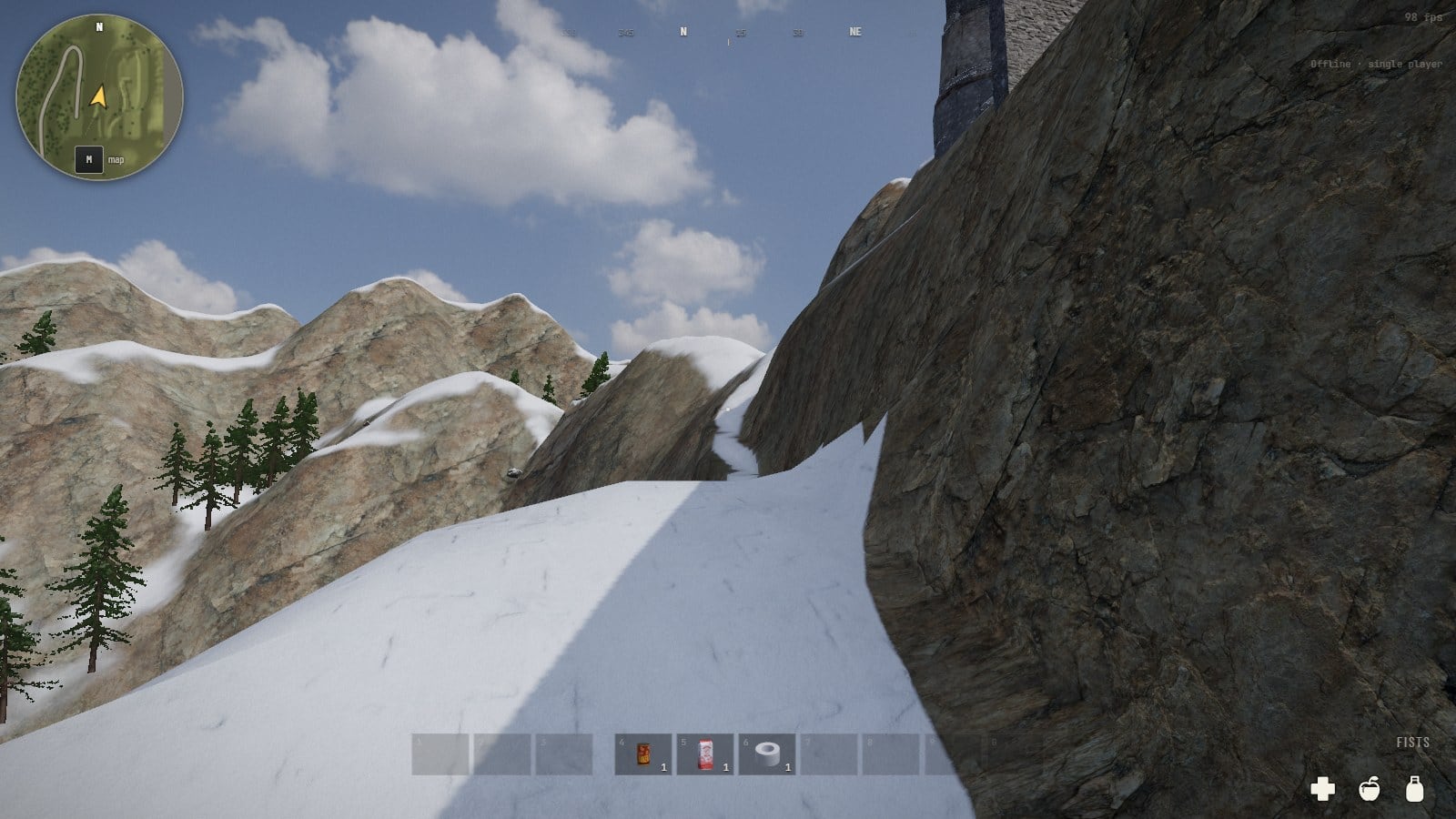 A narrow shelf of snow running along a rock face that stands nearly upright on the right and falls away on the left, bare mountains and a few pines beyond